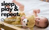 A baby is lying on a white surface, holding a teddy bear. Text overlays highlight product features. Produktbild-Vorschau
