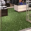 A retail store interior with a floor covered in a grass and daisy print, displaying folded clothing on shelves and display units. Produktbild-Vorschau