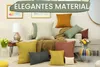 A collection of decorative pillows arranged on and around a sofa, with a lamp and artwork in the background. Produktbild-Vorschau