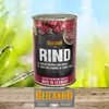 A can of dog food is shown in a natural outdoor setting with grass and a blue sky. Produktbild-Vorschau