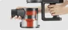 A hand holding the dustbin of a cordless vacuum cleaner, with another hand holding the handle. Produktbild-Vorschau
