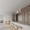 A modern kitchen and dining area with pendant lights, a marble island with bar stools, a dining table with chairs, and a refrigerator. Produktbild-Vorschau