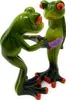 Two green ceramic frog figurines are shown against a white background. One frog is bending over and appears to be looking at or adjusting the purple underwear of the other frog, which is standing upright. Produktbild-Vorschau