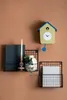A cuckoo clock and two wall-mounted baskets are displayed on a brown wall. Produktbild-Vorschau