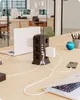 A power strip tower is shown on a wooden desk, surrounded by laptops and charging cables, in an office setting. Produktbild-Vorschau