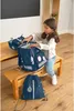 A young girl is packing a navy blue school backpack on a wooden bench. Voir les images du produit