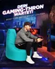 A man is playing a video game while sitting on a large turquoise beanbag chair in a dimly lit room with a cityscape visible through a window. Produktbild-Vorschau