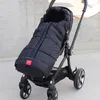 A black stroller with a black footmuff attached, placed outdoors on a concrete surface. Produktbild-Vorschau