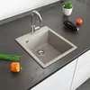 A kitchen sink with a faucet, on a dark countertop, with some vegetables and a plant nearby. Náhled obrázku produktu