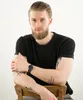 A man wearing a black t-shirt and a watch is sitting on a chair. Podgląd zdjęcia produktu