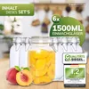 A collection of glass jars filled with peaches, with fresh peaches in the foreground, set against a blurred kitchen background. Produktbild-Vorschau