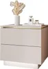 A modern beige nightstand with two drawers and gold trim, decorated with a vase of dried flowers and two perfume bottles. Produktbild-Vorschau