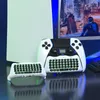 A gaming console and controllers with attached keyboards are displayed on a reflective surface, with a city skyline visible on a screen in the background. Produktbild-Vorschau