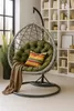 A hanging chair with a green cushion and a striped pillow is placed in a room with a bookshelf in the background. Voir les images du produit