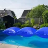 Three blue inflatable pool cushions floating on the surface of a swimming pool, with houses and trees in the background. Produktbild-Vorschau