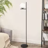 A modern black floor lamp with a white glass shade is placed next to a gray armchair with a beige throw blanket and a tall bookshelf filled with books. Anteprima dell’immagine prodotto