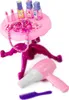 A pink toy vanity table with accessories, including lipsticks, necklaces, perfume bottles, a hairdryer, and a comb, set against a white background. Produktbild-Vorschau