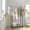 A double-tiered rolling garment rack filled with clothing and accessories, placed near a window with plants. Anteprima dell’immagine prodotto
