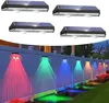 Four solar wall lights are shown at the top, and a row of these lights are installed on a fence at the bottom, illuminating the fence and ground with colorful lights. Produktbild-Vorschau