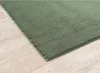 A close-up, angled view of a green rug on a light wood floor. Produktbild-Vorschau