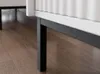 A close-up view of the legs and bottom edge of a white cabinet with a black metal frame, resting on a wooden floor. Voir les images du produit