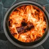 A close-up view of a fire pit with burning logs. Produktbild-Vorschau