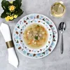 A festive Christmas table setting with a soup bowl, plates, a napkin, a glass of white wine, and a small potted plant. Náhled obrázku produktu