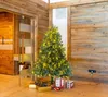A decorated Christmas tree with presents underneath, set in a room with wooden walls and a glass door. Produktbild-Vorschau