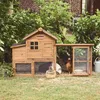 A wooden chicken coop with an attached run, set in a garden with lush greenery and a brick building in the background. Produktbild-Vorschau
