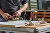 A person is using a woodworking tool on a piece of wood on a workbench. There are clamps holding the wood in place. Náhľad obrázku produktu