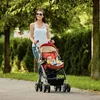 A woman pushes a stroller with a baby in it along a paved path in a park. Anteprima dell’immagine prodotto