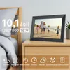 A digital photo frame displaying a family on a beach, placed on a bedside table next to a bed. Produktbild-Vorschau