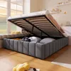 A bed with its storage compartment open, revealing items inside, in a room with a window and wooden floor. Produktbild-Vorschau