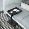 A black marble-patterned C-shaped side table with a cup of coffee and a magazine is placed next to a gray sofa on a striped rug. Produktbild-Vorschau