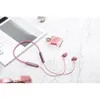 A pair of rose pink in-ear headphones with a neckband, placed on a marble-like surface next to a bottle of perfume and a magazine. Produktbild-Vorschau