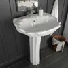 A white ceramic pedestal sink with a decorative basin and fluted pedestal, set against a dark gray paneled wall. Podgląd zdjęcia produktu