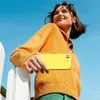 A young woman holding a yellow phone case outdoors. Produktbild-Vorschau