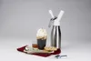 A whipped cream dispenser with a glass of coffee and a cookie on a red napkin. Produktbild-Vorschau