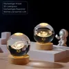 Two illuminated crystal spheres with celestial engravings on wooden bases, with a small astronaut figurine in the background. Produktbild-Vorschau