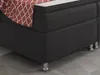 A close-up view of the corner of a black box spring bed with a red and white patterned throw blanket draped over it. Produktbild-Vorschau