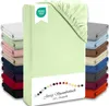 A stack of folded fitted sheets in various colors, with a light green fitted sheet prominently displayed in the foreground. Produktbild-Vorschau