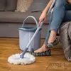 A person is cleaning a wooden floor with a mop and bucket. Podgląd zdjęcia produktu