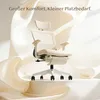 A white ergonomic office chair is displayed on a pedestal, surrounded by flowing fabric. Produktbild-Vorschau
