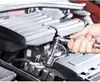 A person's hand is using a socket wrench to work on a car engine. Produktbild-Vorschau