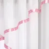 A close-up view of white sheer curtains with pink satin ribbon trim. Produktbild-Vorschau