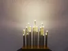 A decorative light fixture with multiple LED lights resembling candles, casting a warm glow on a textured wall. Produktbild-Vorschau