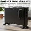A black electric convector heater is shown on a light-colored wooden floor, with a potted plant and a blurred sofa in the background. Produktbild-Vorschau