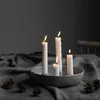 A candle holder with four lit candles and pinecones on a draped table. Produktbild-Vorschau