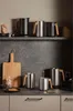 A kitchen counter with various kitchenware, including kettles, a cutting board, and plates. Anteprima dell’immagine prodotto
