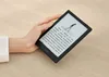 A hand holding a black e-reader with text and an illustration on the screen, resting on a wooden table. Produktbild-Vorschau